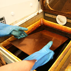 The copper plate is immersed into the bath of ferric chloride solution. The first etching process has started.