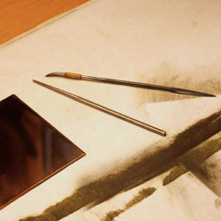 The copper plate together with the two tools needed. To the left is a steel needle and to the right a combined scraper and burnisher - see the different ends of the right tool. The burnisher is a gently curved steel blade.