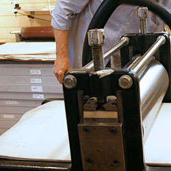 The steel roller presses down the two woolen felters which in turn press down the soft damp copper-plated paper into the scratches where the paper picks up the color.