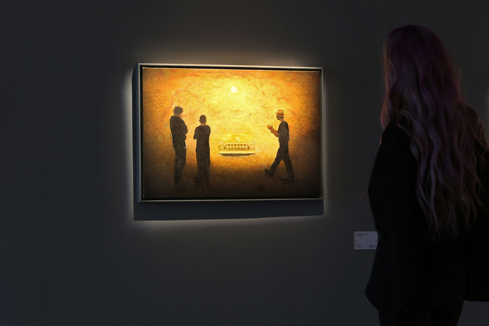 En betraktare av målningen Besökaren #2 av John E Franzén. Tre män och en bil i guld.