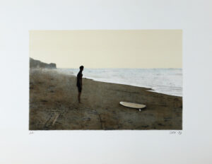 Litografi Surfer av John E Franzén - En man som står på en strand intill en surfingbräda.